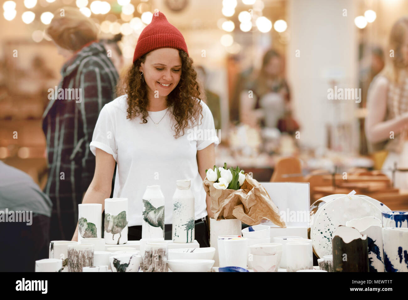 Young hipster woman selling behind counter with her ceramics and porcelain hand-painted at local market of craftsmen, small business Stock Photo