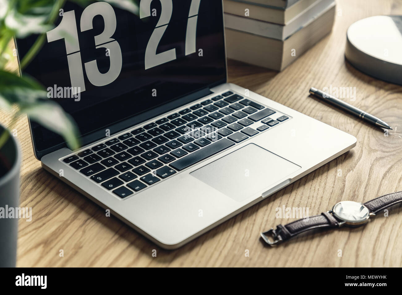 Close-up of a laptop showing time, watch, pen and books on a wooden desk Stock Photo