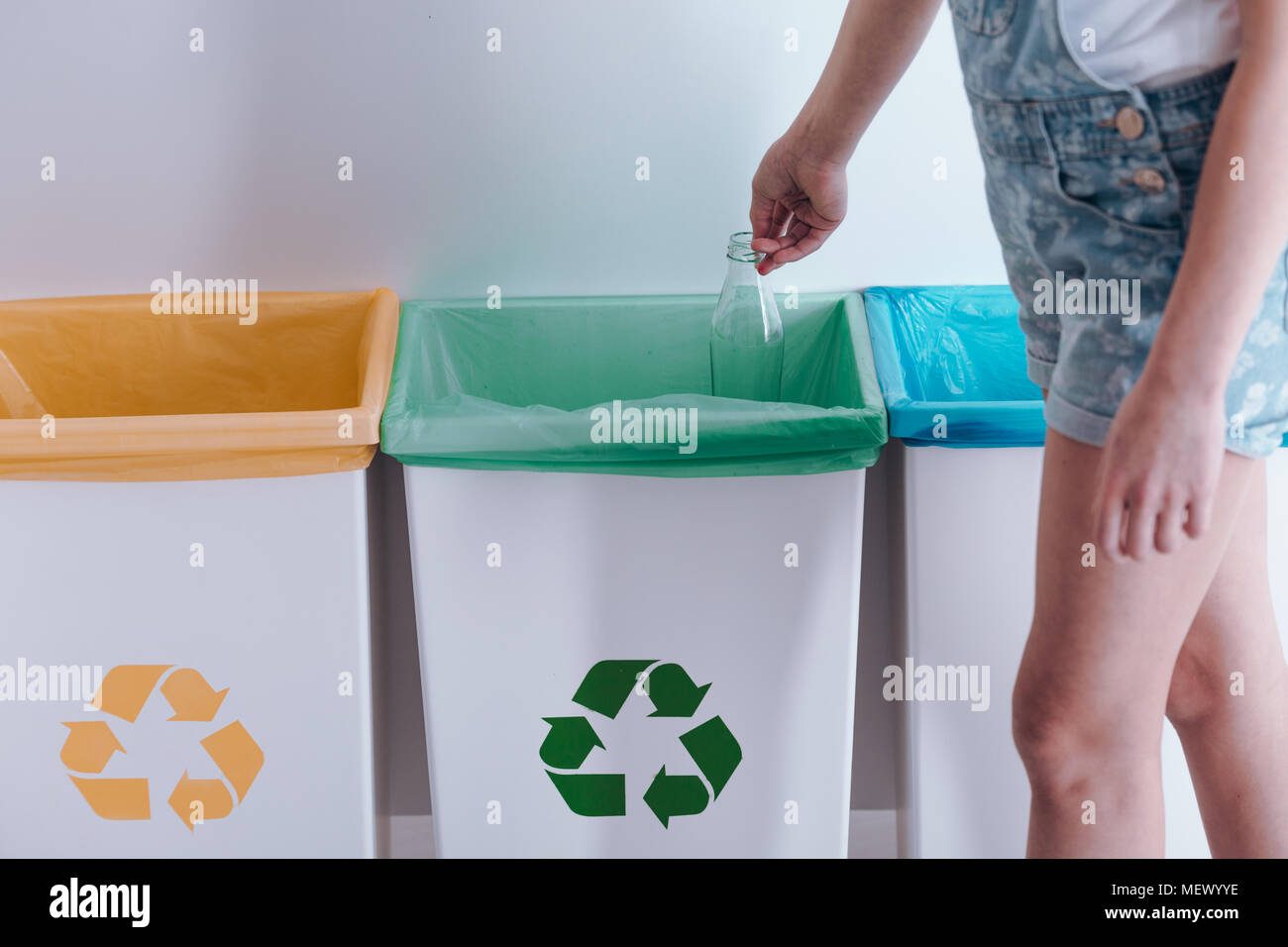 Child throwing a glass bottle into green container for recycling Stock Photo