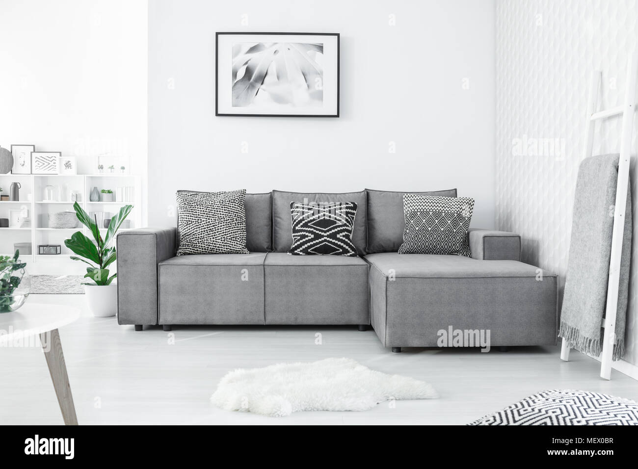 Grey corner couch with three patterned pillows standing in bright living room interior with