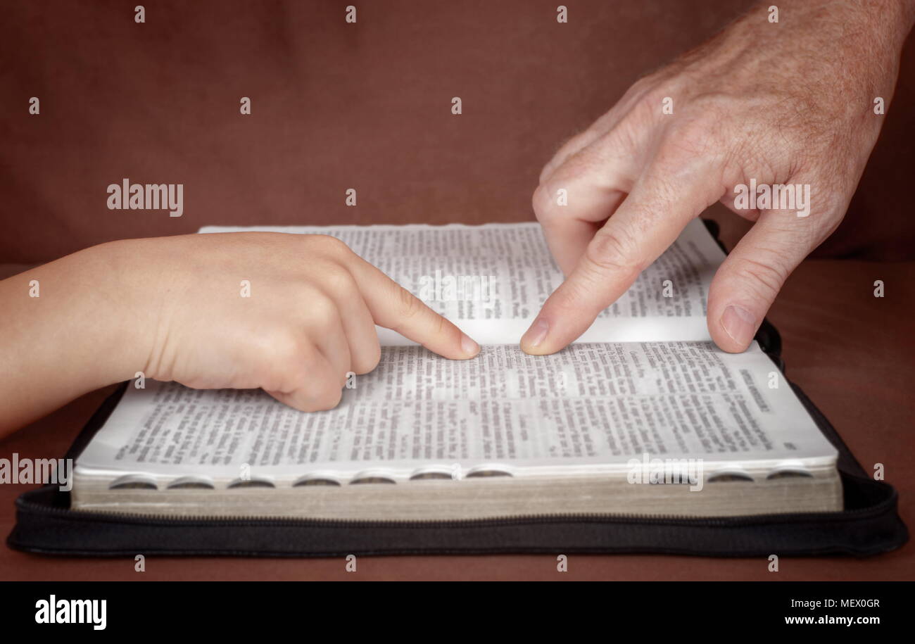 Hand of man pointing something to a child in the Bible book. Teaching a disciple from the Bible. Stock Photo