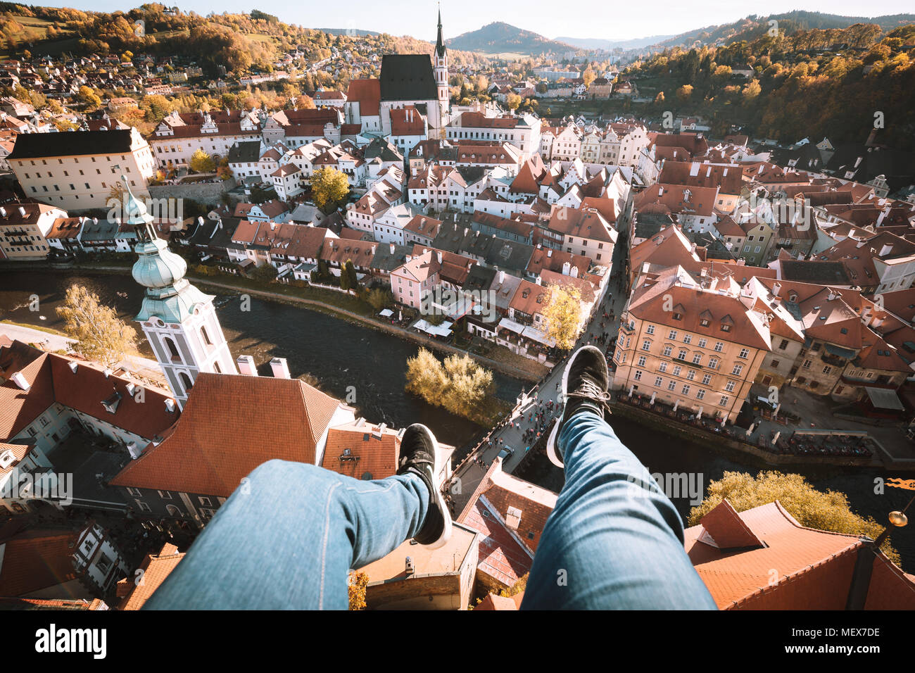 Aerial birds eye view of young rooftop climber sitting on the edge of a high rise tower dangling his feet high above the old town of Cesky Krumlov Stock Photo