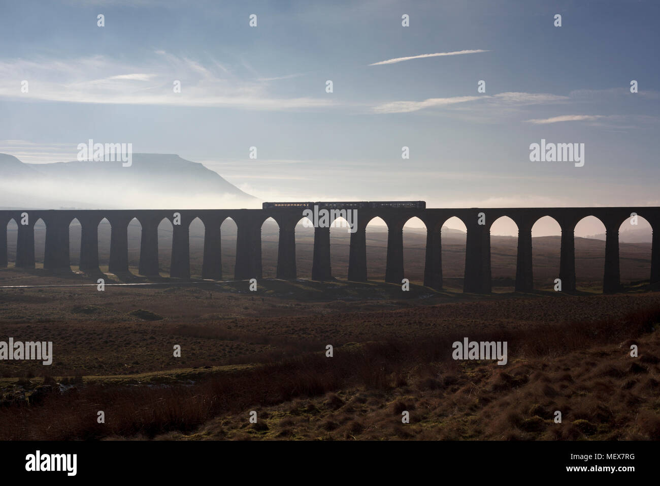 A Northern rail class 153 + 156 sprinter trains cross Ribblehead viaduct on the Settle to Carlisle railway with a misty Ingleborough behind Stock Photo