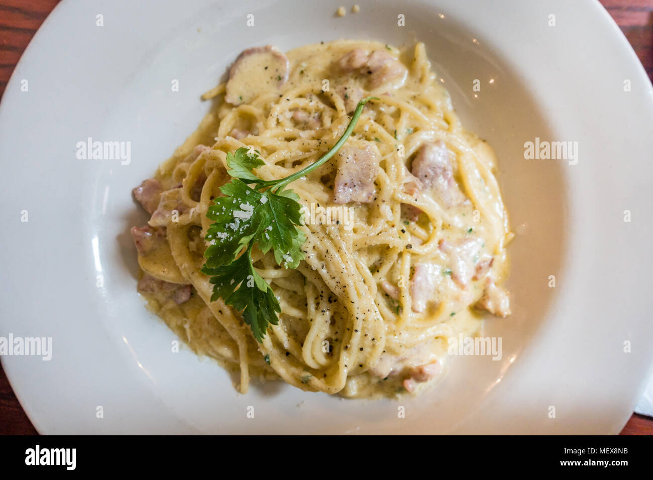 A close up view of a bowl of Spaghetti Carbonara garnished wiht a sprig of parsely. Stock Photo