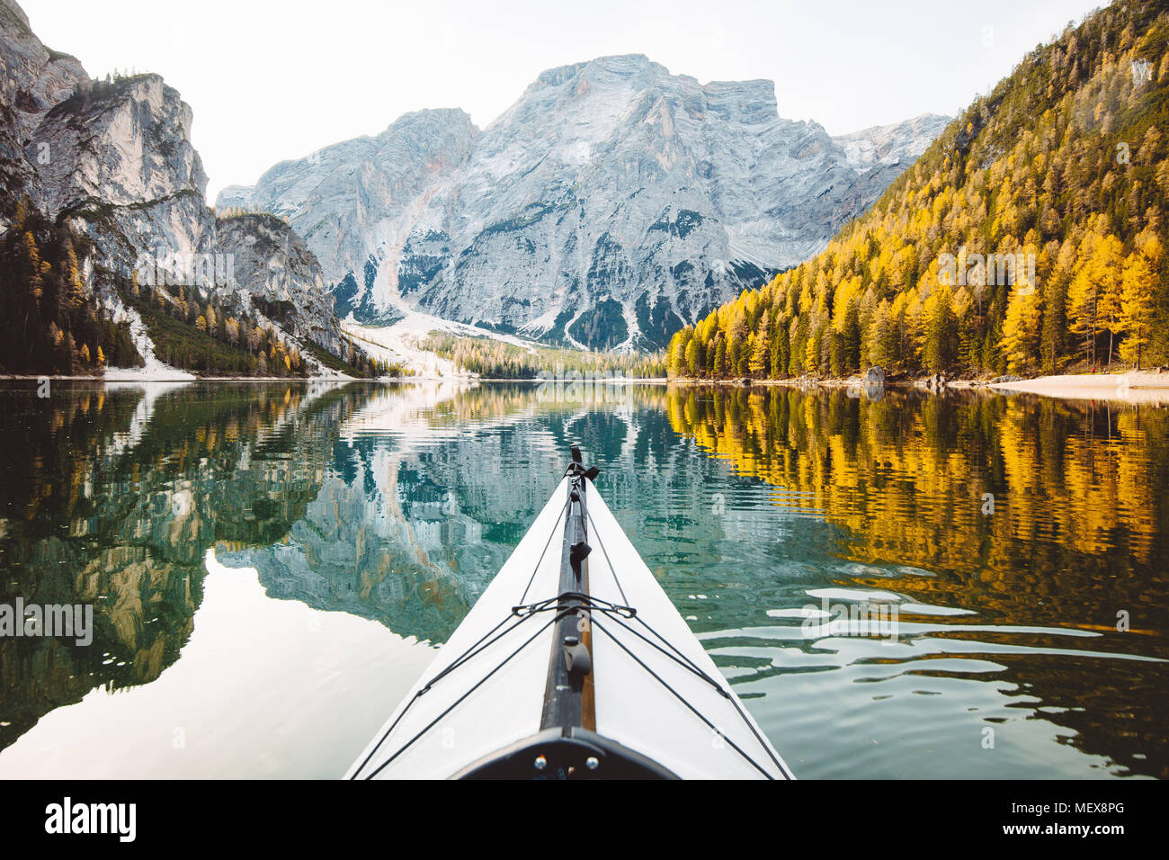 Beautiful view of kayak on a calm lake with amazing reflections of mountain peaks and trees with yellow autumn foliage in fall, Lago di Braies, Italy Stock Photo