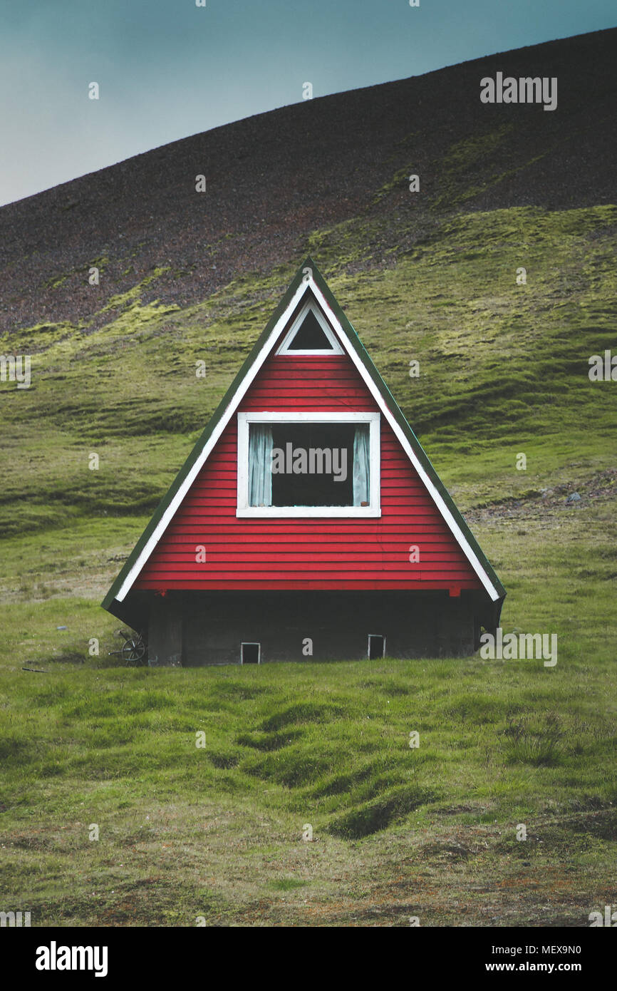 Beautiful view of traditional red A-frame cabin with green meadows and dark moody clouds on a summer day in Iceland Stock Photo