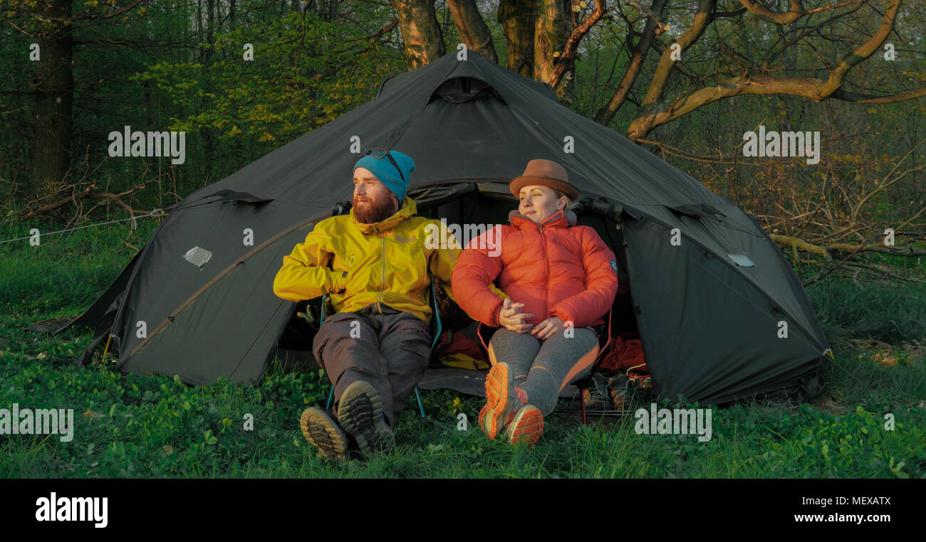 outdoors couple (man and woman) sitting in front of a tent on camping ...