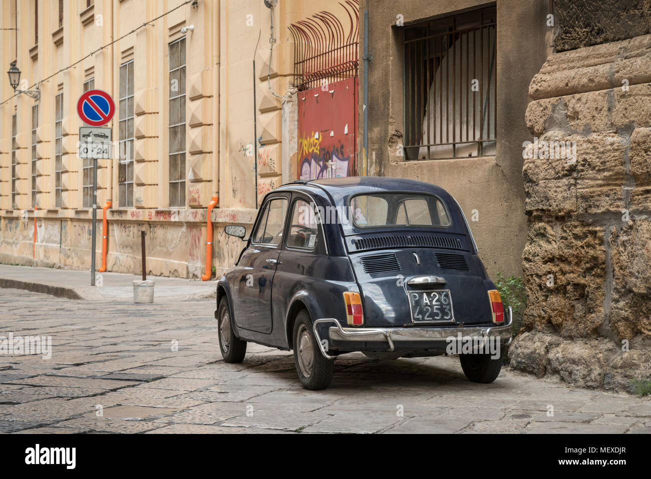 An original old blue Fiat 500 car parked in a back street of Palermo, Sicily, Italy, a 24 hour tow away zone sign in front. Stock Photo