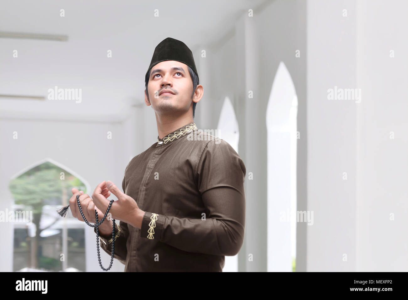 Young asian muslim man with prayer beads praying in the mosque Stock Photo