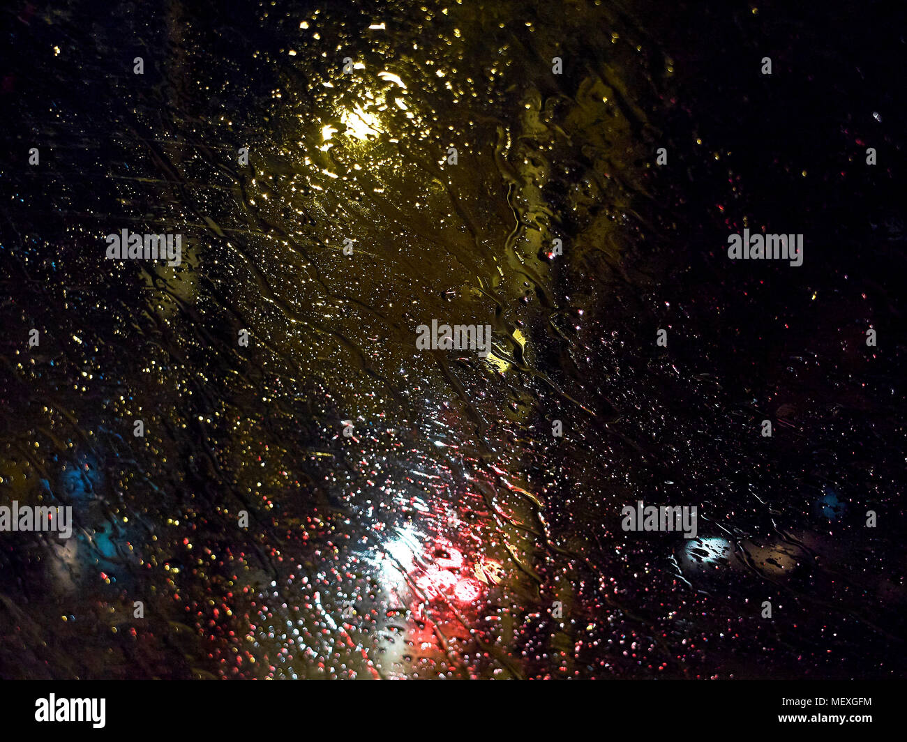 Raindrops on the car window at night illuminated by street lights during heavy rain background Stock Photo