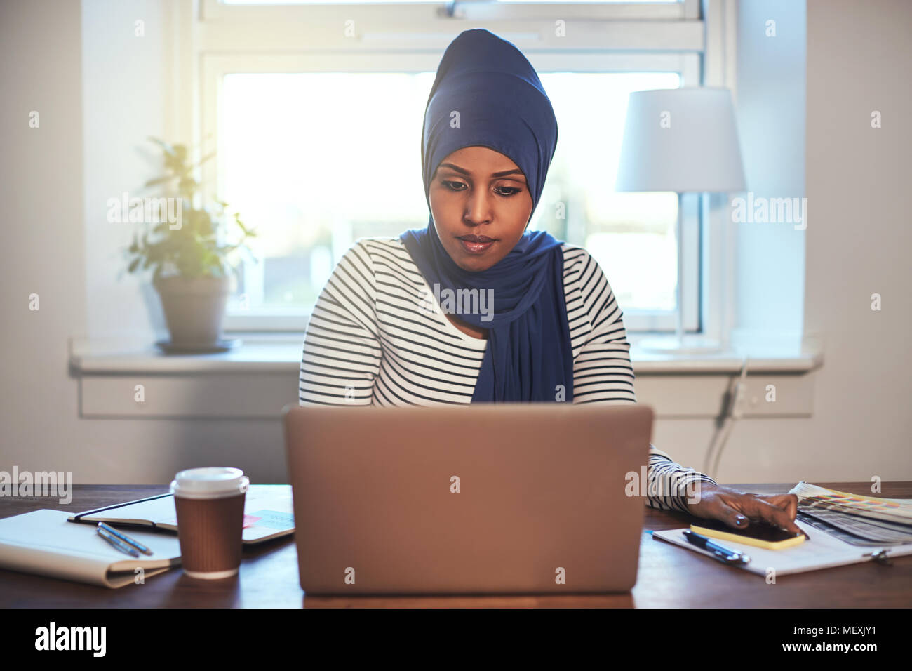 Focused young Arabic female entrepreneur wearing a hijab working online ...