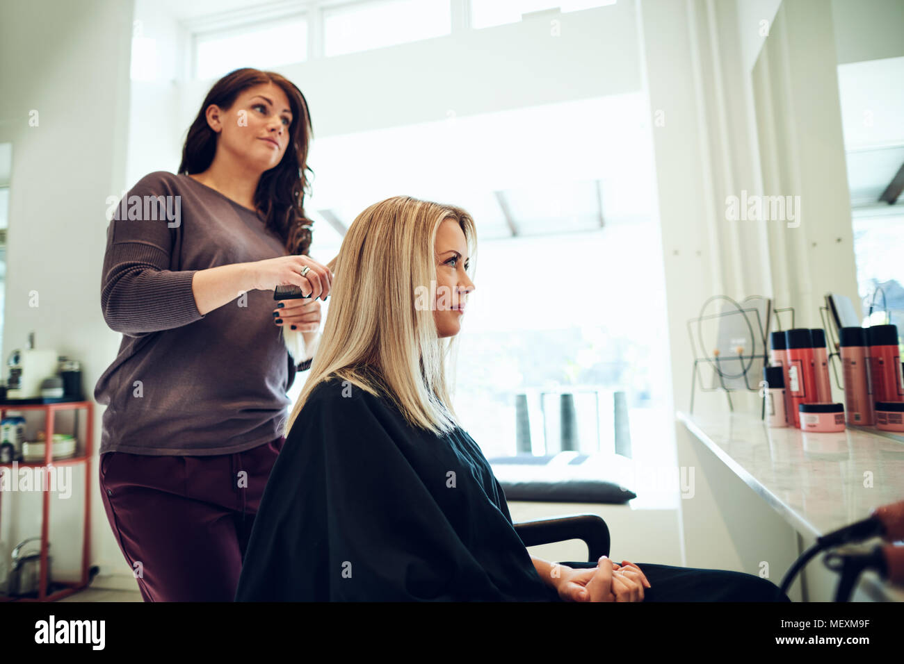 Hairdresser Styling The Hair Of A Young Blonde Woman Sitting In A
