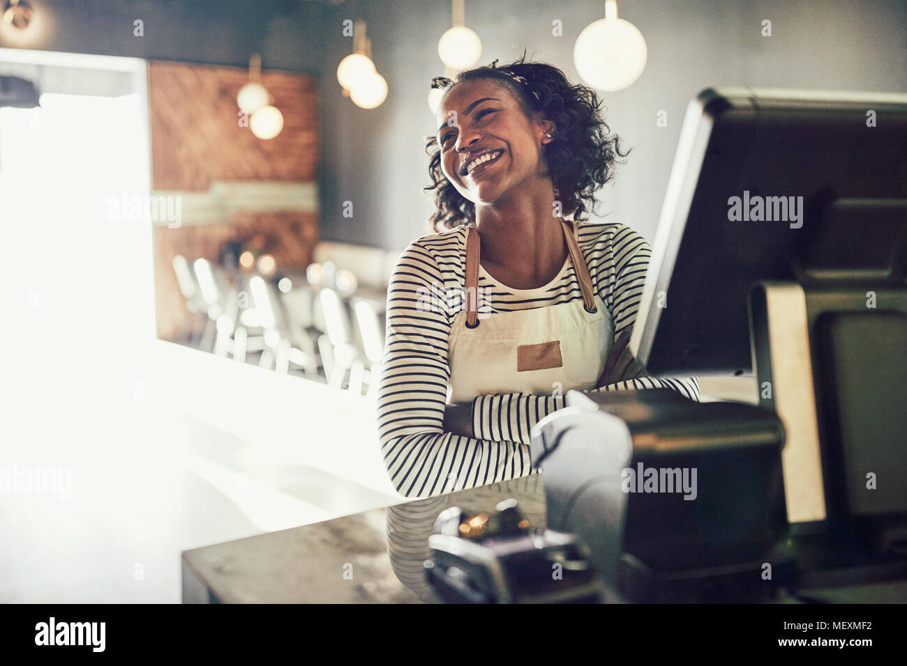 Young African waitress laughing while standing by a point of sale terminal in a trendy restaurant Stock Photo