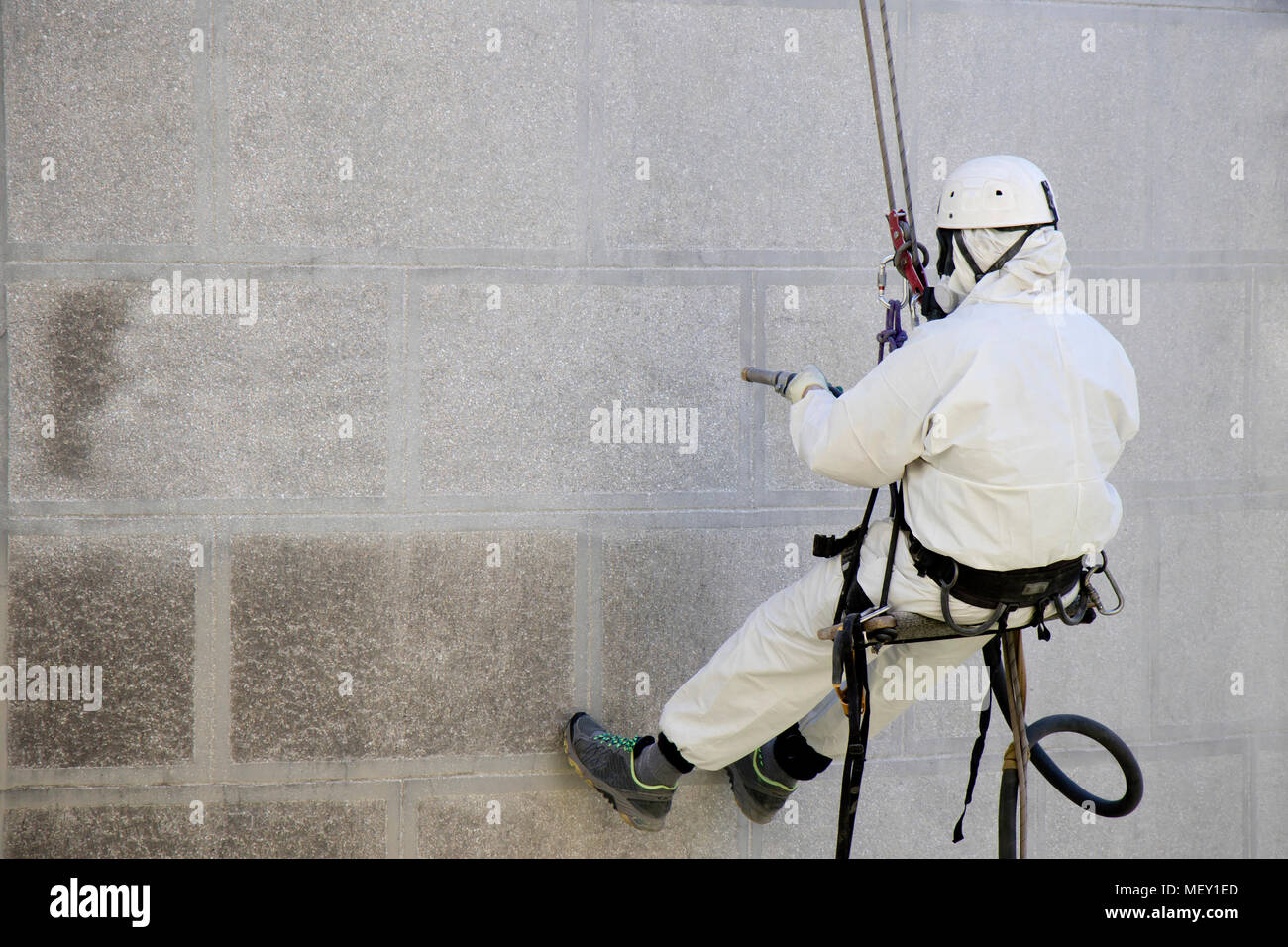 Rope access facade maintenance; A worker wearing a protective gear cleaning a stone exterior with sandblasting equipment Stock Photo