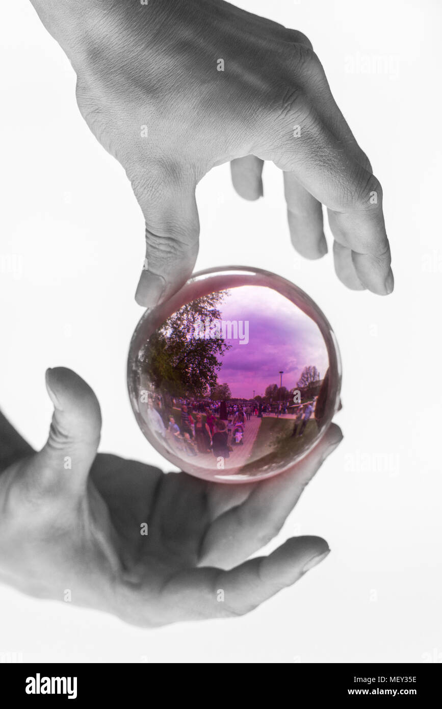 man with red hands dressed as the devil holds and plays with an isolated glass crystal ball containing reflections of people Stock Photo