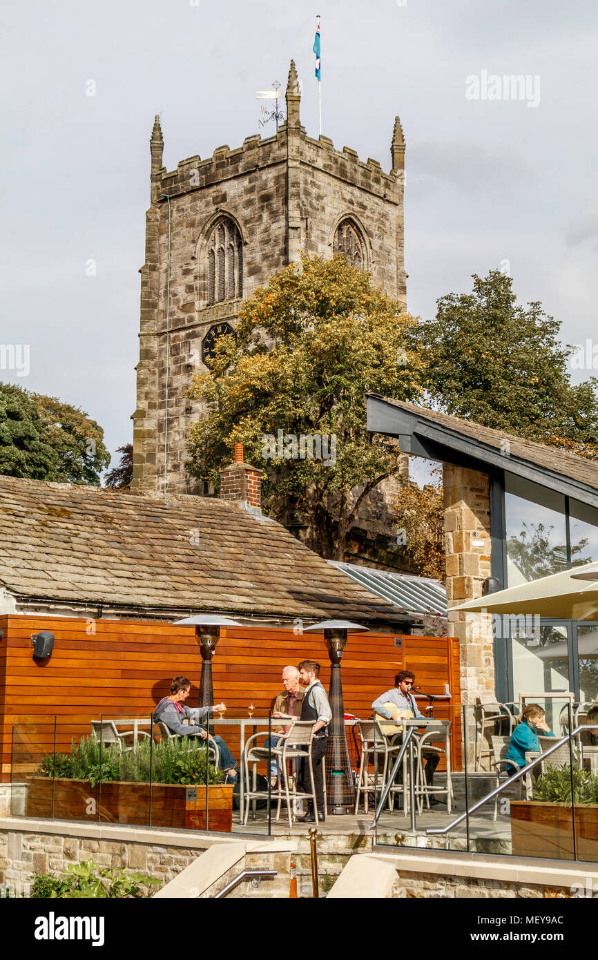 The tower of the 14thC medieval, Grade 1, Anglican, Holy Trinity Church at Skipton, North Yorkshire, UK. Restaurant patio in the foreground. Stock Photo