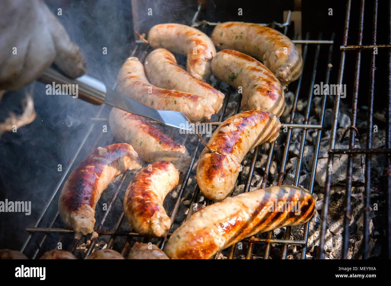 Fresh sausage. Hot dogs grilling outdoors on a gas barbecue grill. Male cook flips grilled sausages on open fire. Stock Photo