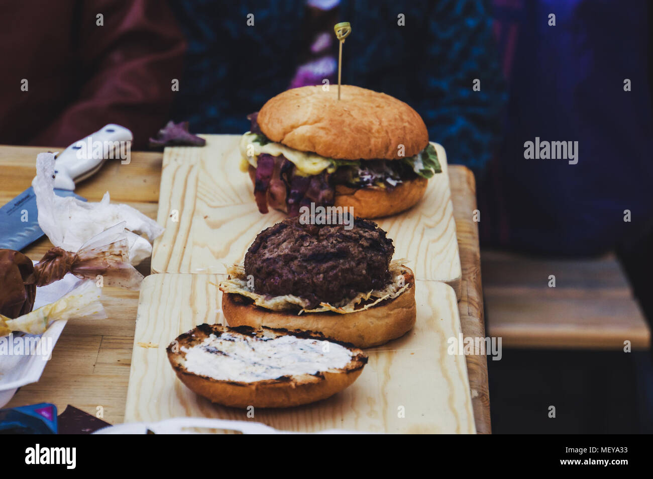 Burger hamburger on a dark background with fresh vegetables. Preparing sandwiches at home on the kitchen table. The Patty bun on a wooden Board. Stock Photo