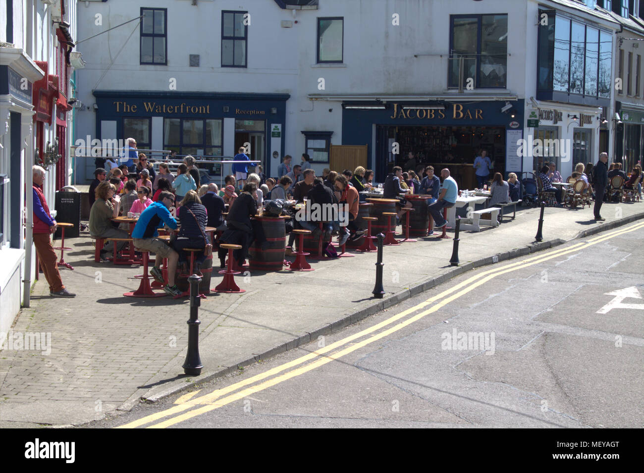 people eating and drinking outside the pubs and restaurants of baltimore sea front. Baltimore is a popular tourist and holiday destination in ireland. Stock Photo
