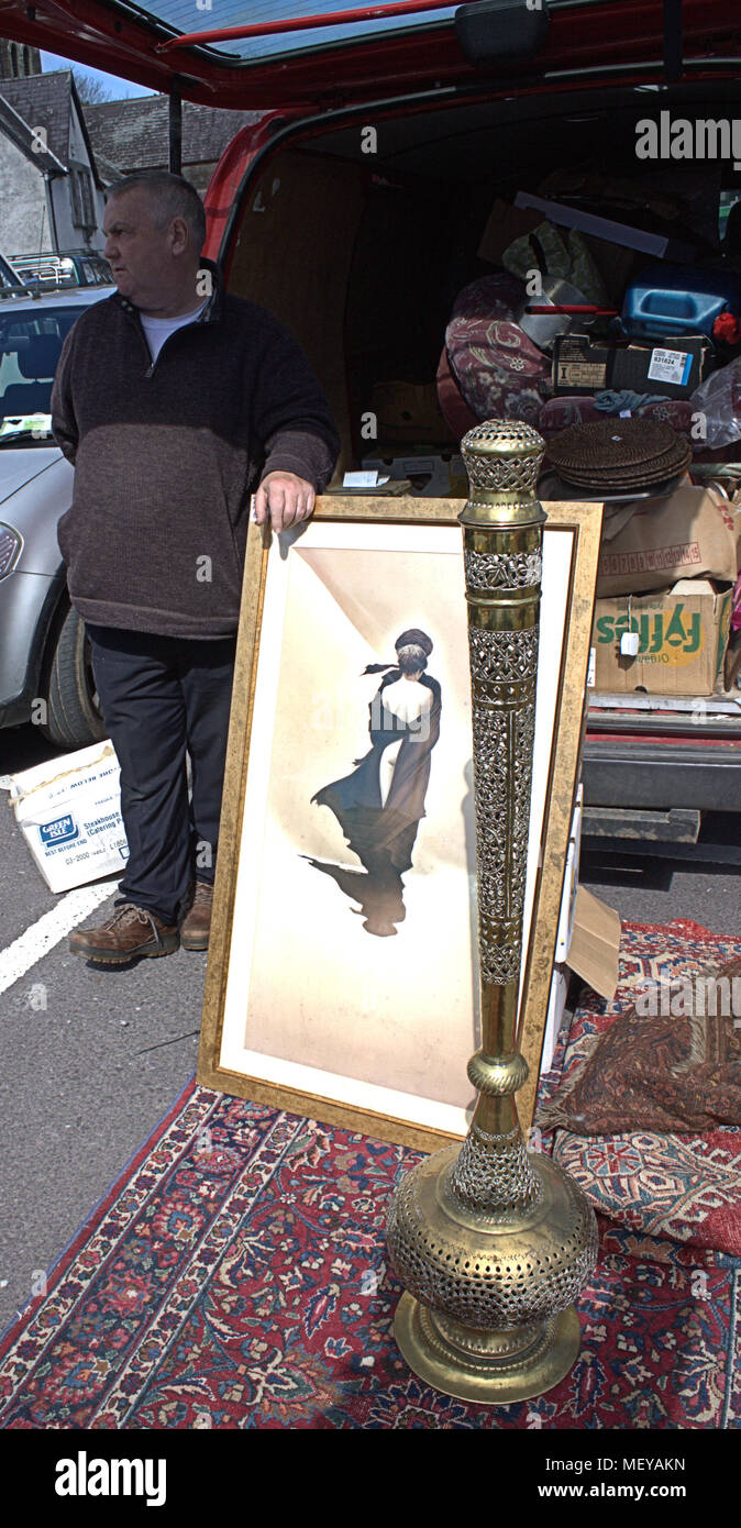 Male market trader holding a framed picture, standing behind a large brass incense burner he is selling, both items are on heavily patterned rug. Stock Photo