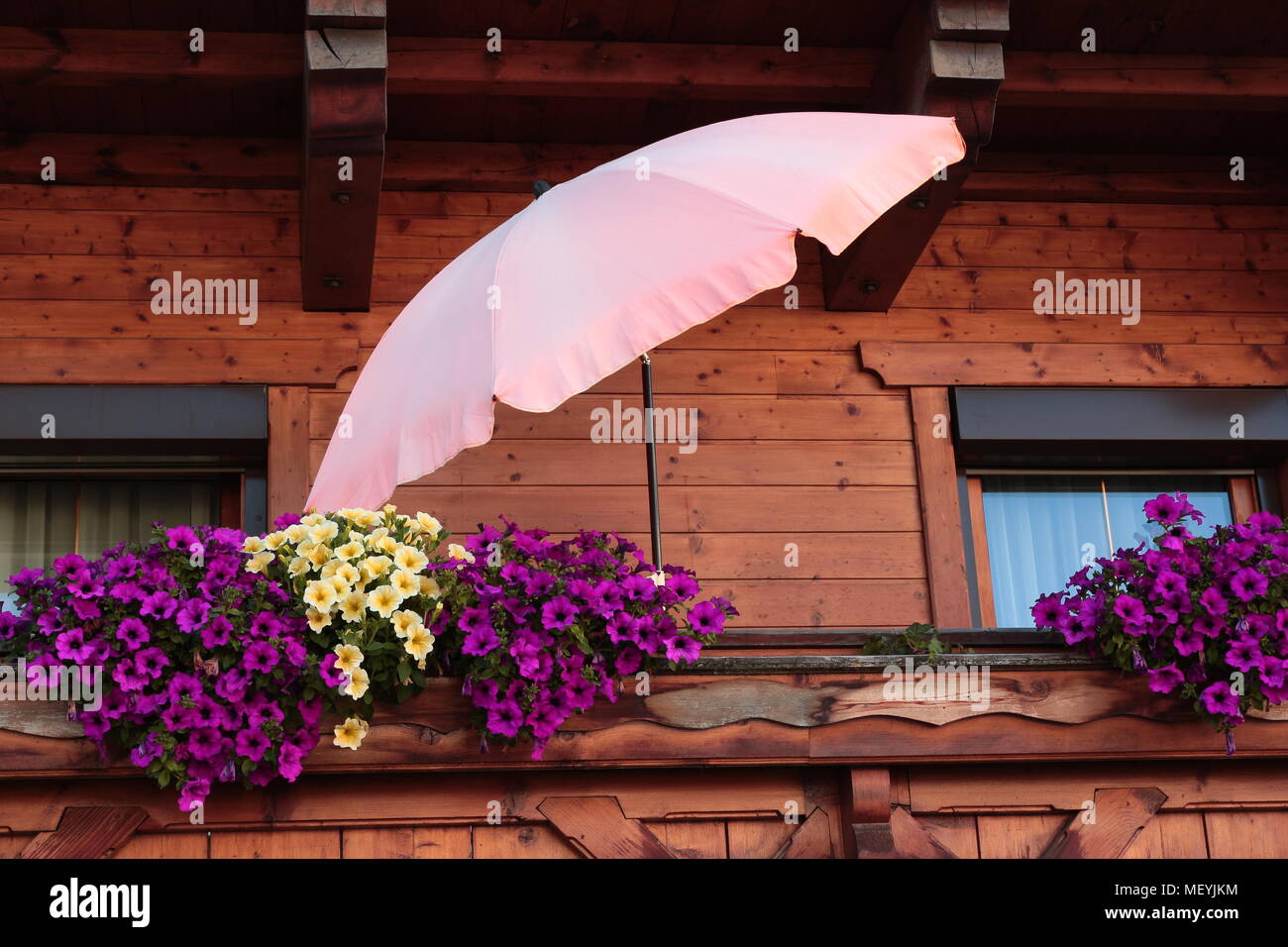 Pink Parasol and purple and yellow flowers on balcony of wooden house Stock Photo
