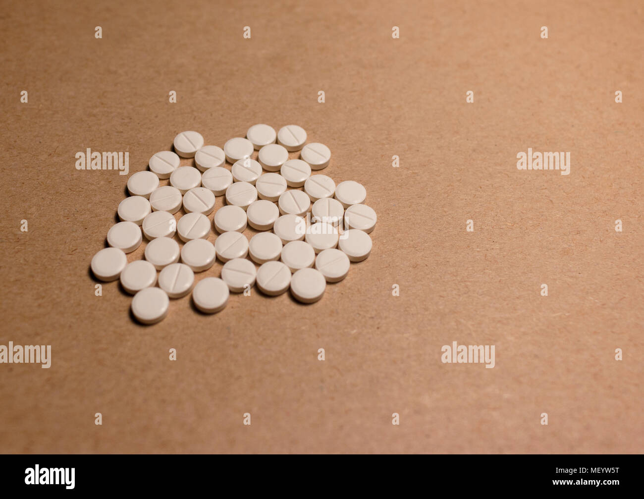 a pile of tablets isolated on a cardboard paper. A pile of beige medical tablets on a brown background Stock Photo