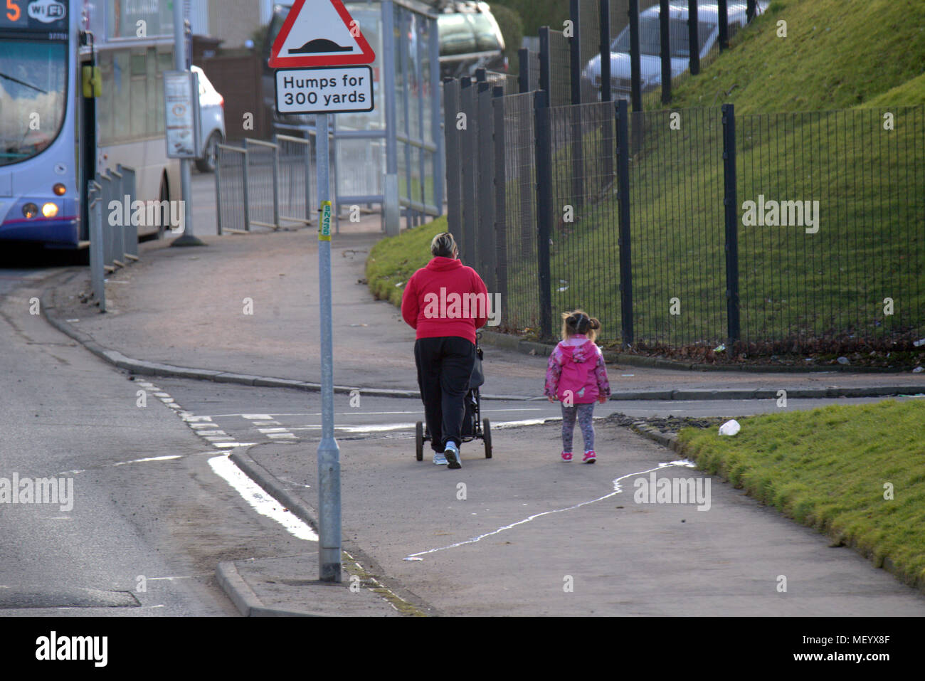 local people single woman mother pushing pram  on street pavement sidewalk  road bus small child Castlemilk, Glasgow, UK Stock Photo