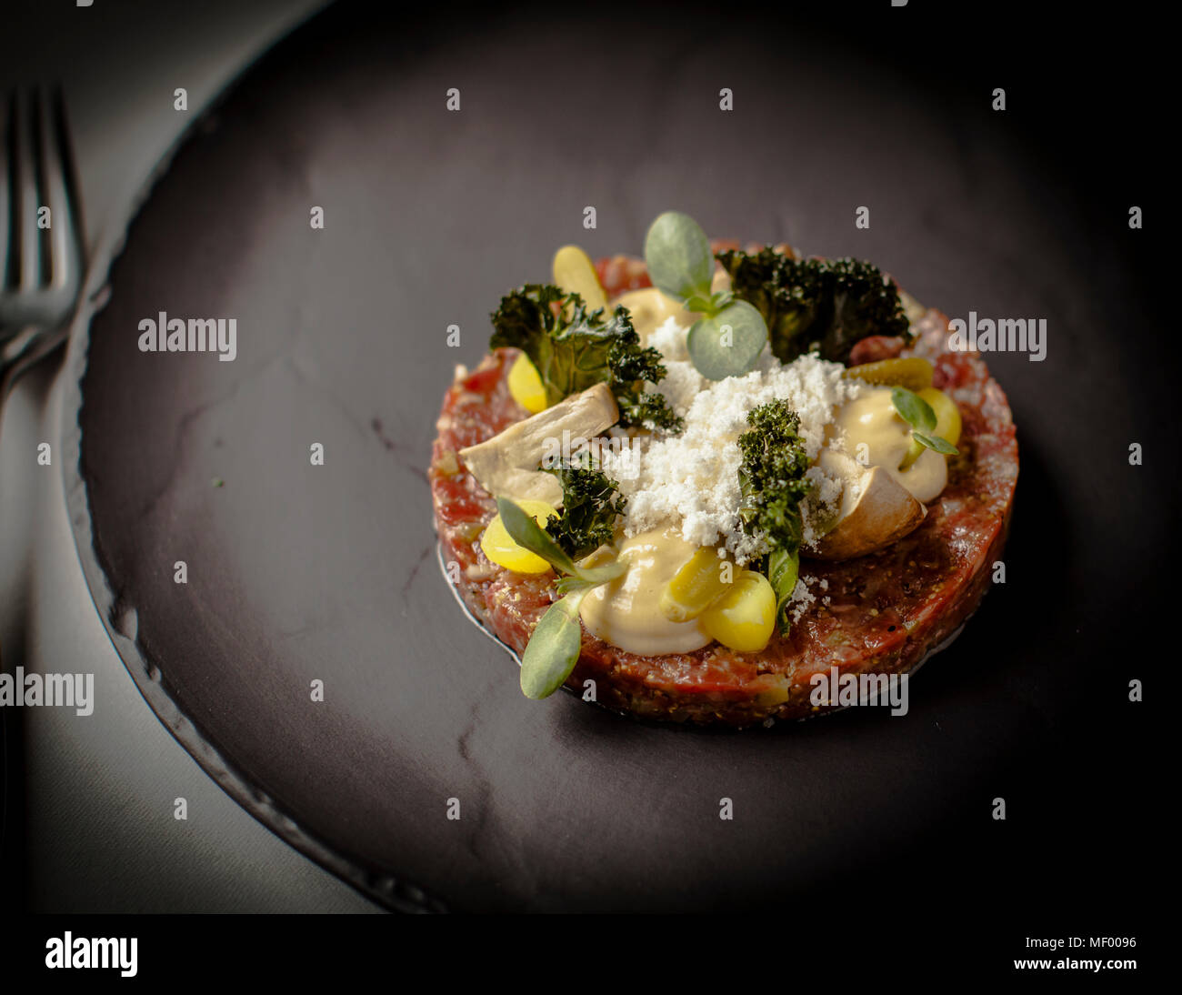 Beef tartare from a local grower, seasoned with shallots, French mustard and Worcestershire sauce and garnished with pickled mushrooms, cucumber and fried kale under powdered nut butter, forms the second course of the four-course menu at head chef Tomasz Purol's restaurant at Hotel Blow Up Hall 5050 in Poznań, Poland. Stock Photo