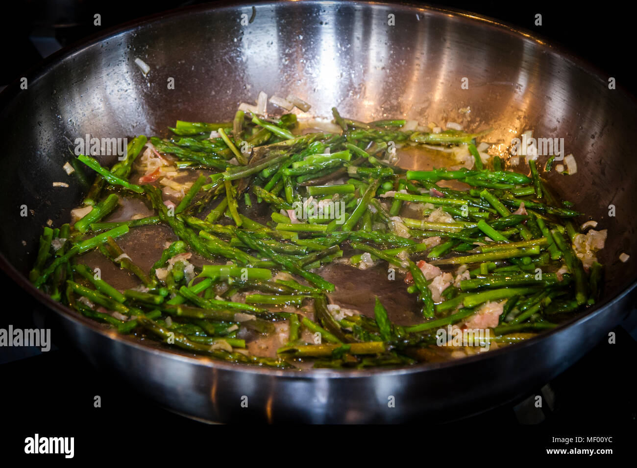 Preparation of asparagus risotto with freshly collected wild asparagus. Preparations for the asparagus risotto: Poirée, and pancetta with olive oil sauté, then add a few pieces of asparagus and black pepper. Foraging the wild asparagus means collecting a delicacy in Tuscany, Italy Stock Photo