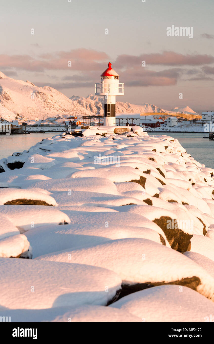 The lighthouse surrounded by snow frames the snowy peaks and the frozen sea Reine Nordland Lofoten Islands Norway Europe Stock Photo