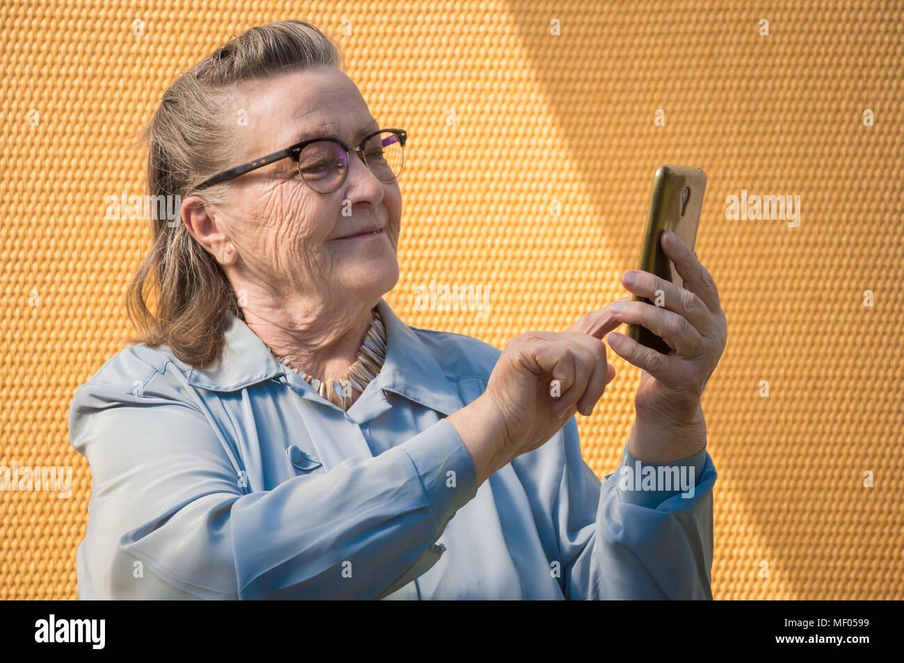 portrait of old lady, grandmother makes selfie outdoors at sun day. modern granny finger touch the touchscreen her phone. she has smartphone in her adult hand. technology lifestyle Stock Photo