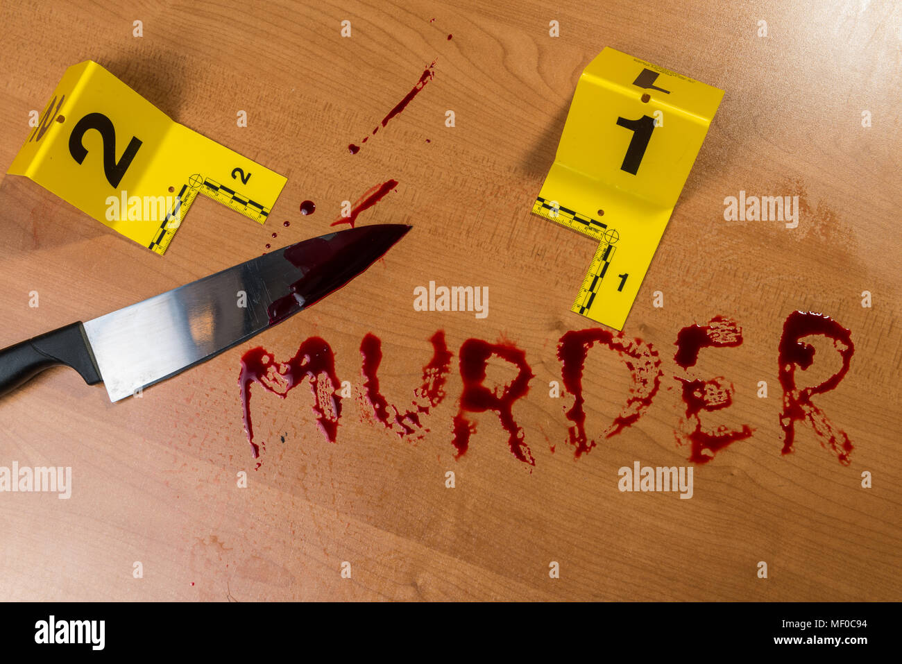 The word “murder” written in blood on a wood surface beside a bloody knife, both marked by crime scene evidence markers. Stock Photo