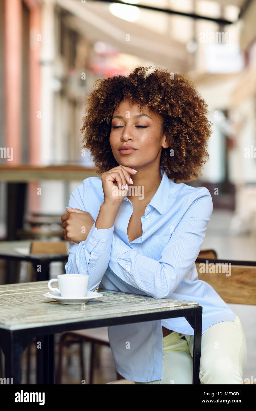 Spain, Andalusia, Malaga.Black woman, afro hairstyle, sitting in a coffee shop. Girl wearing formalwear taking a break. Lifestyle concept. Stock Photo