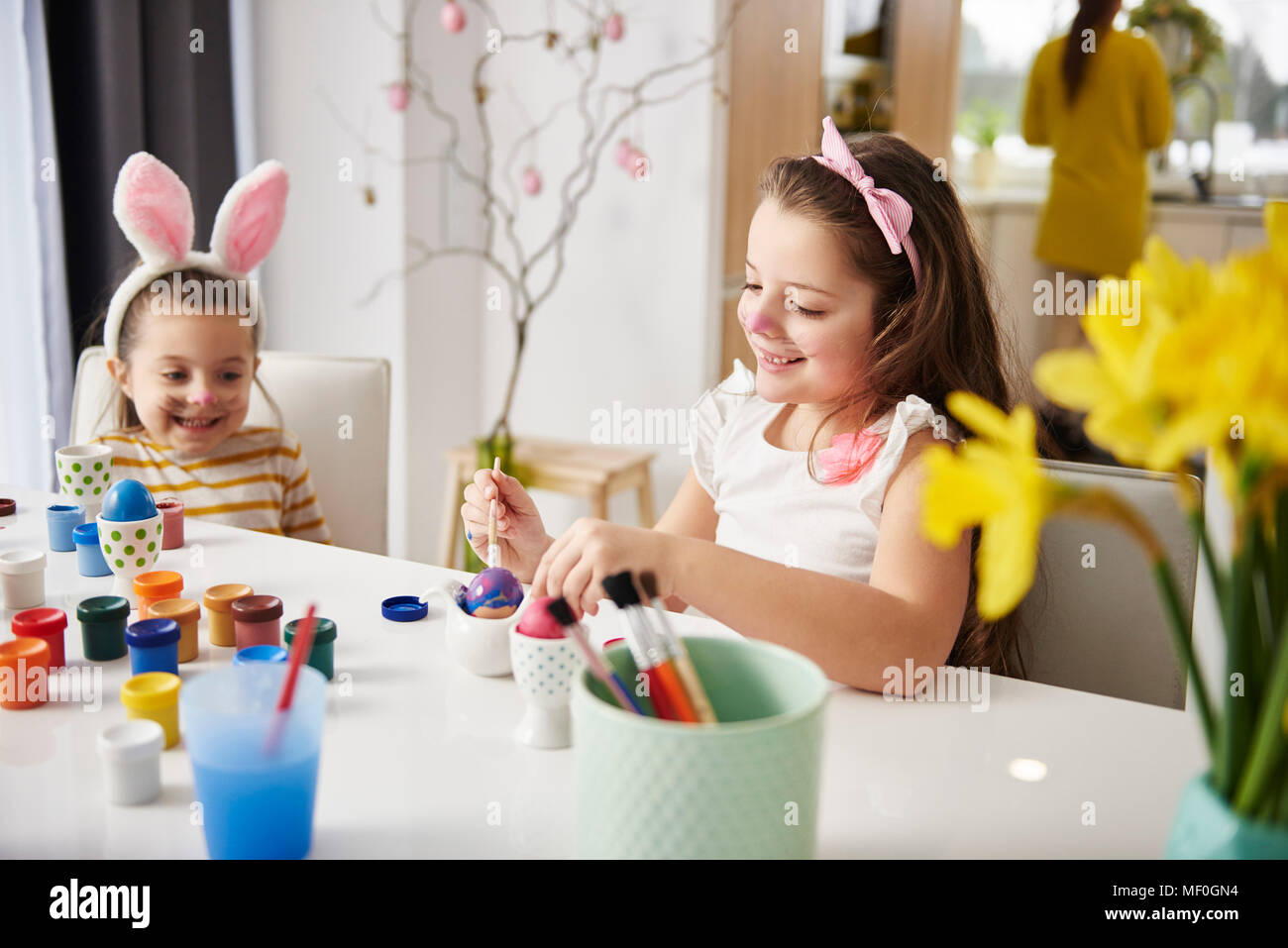 Sisters sitting at table painting Easter eggs Stock Photo