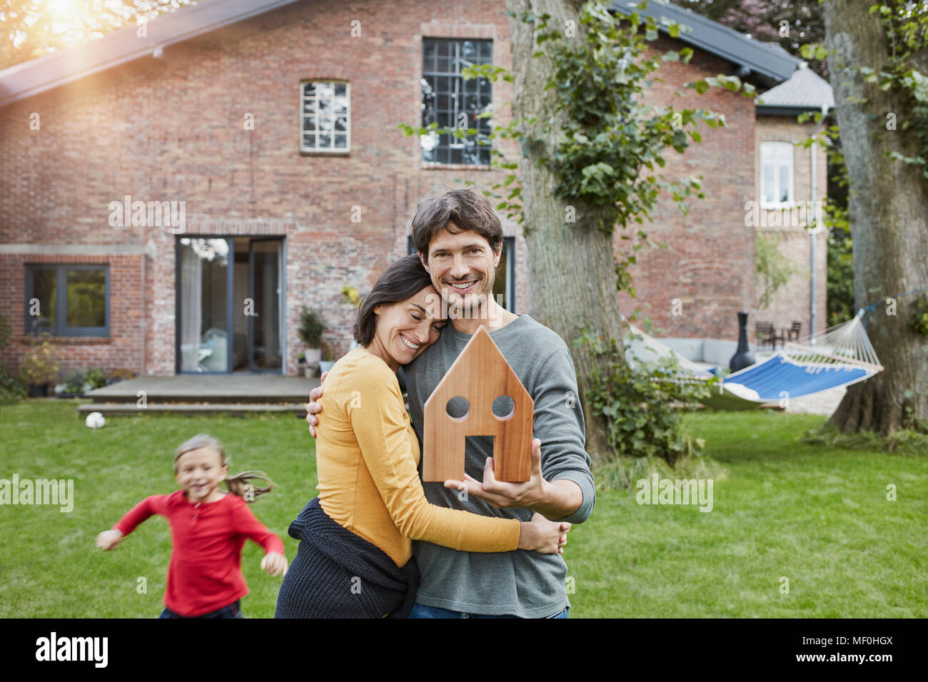 Portrait of smiling couple with daughter in garden of their home holding house model Stock Photo