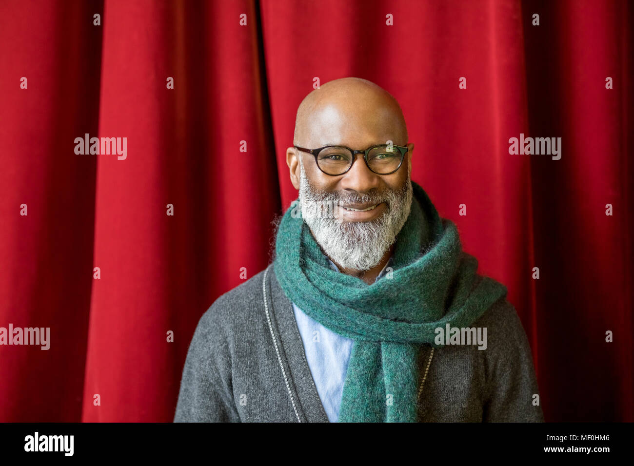 Portrait of smiling man wearing glasses and scarf in front of red curtain Stock Photo