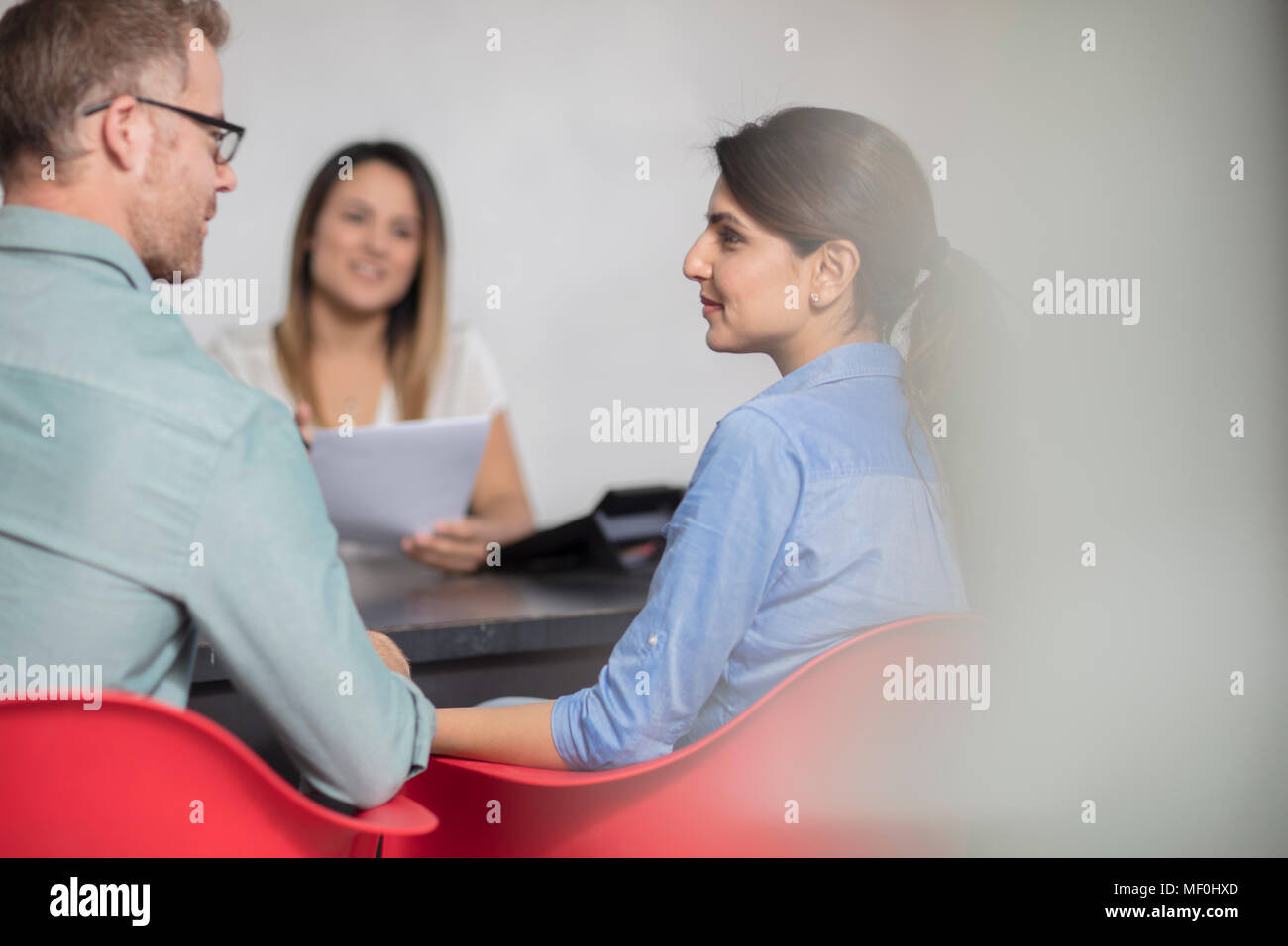 Couple sitting at desk opposite to woman Stock Photo