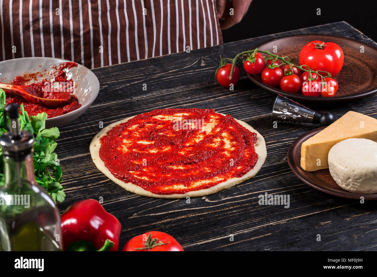 A male hand spreading tomato puree on a pizza base with spoon on an old