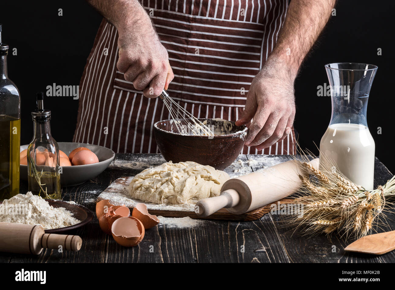 Male chef whipping eggs in the bakery on wooden table. Ingredients for