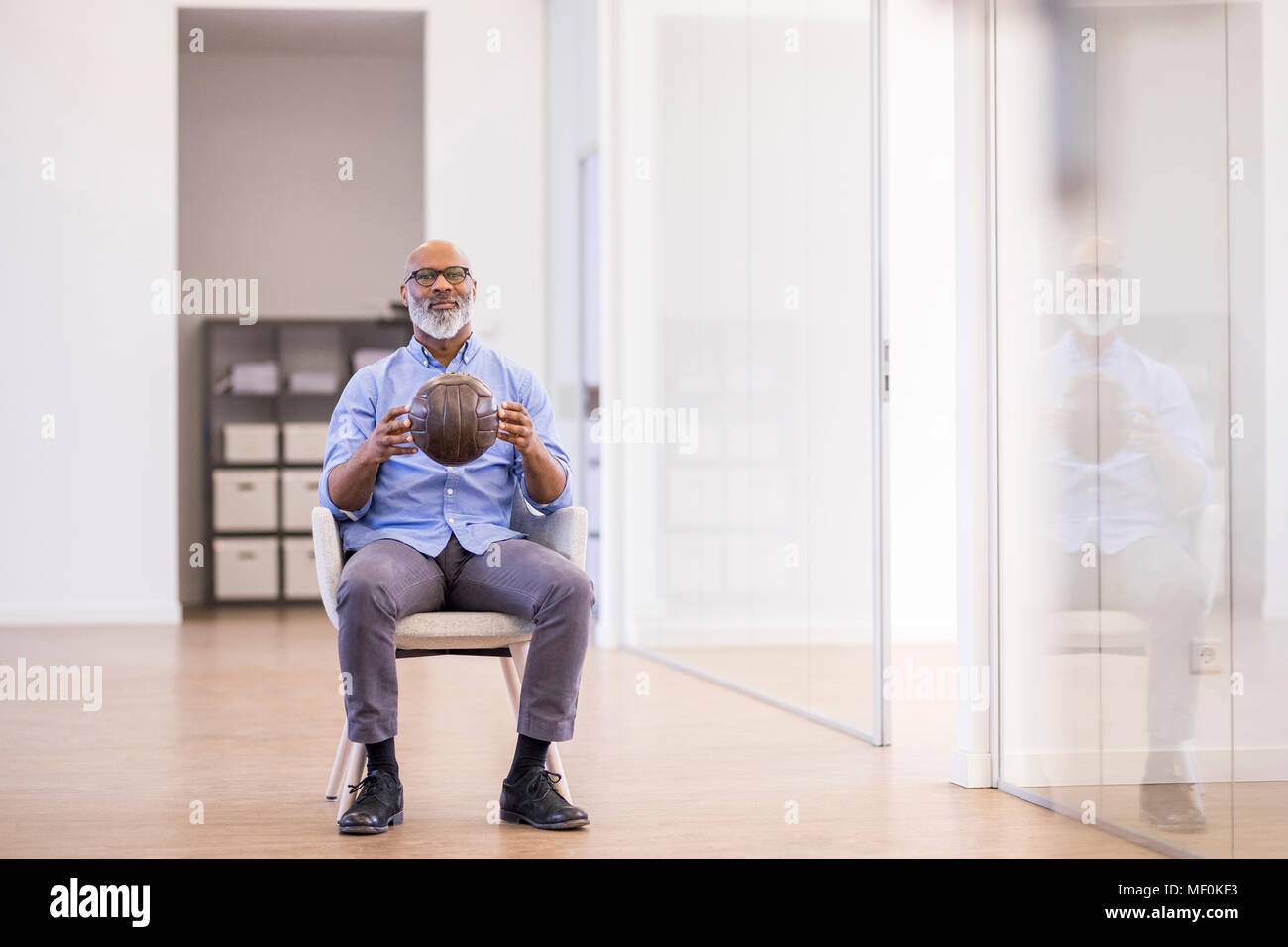 Businessman with leather ball sitting on arm chair in the office Stock Photo