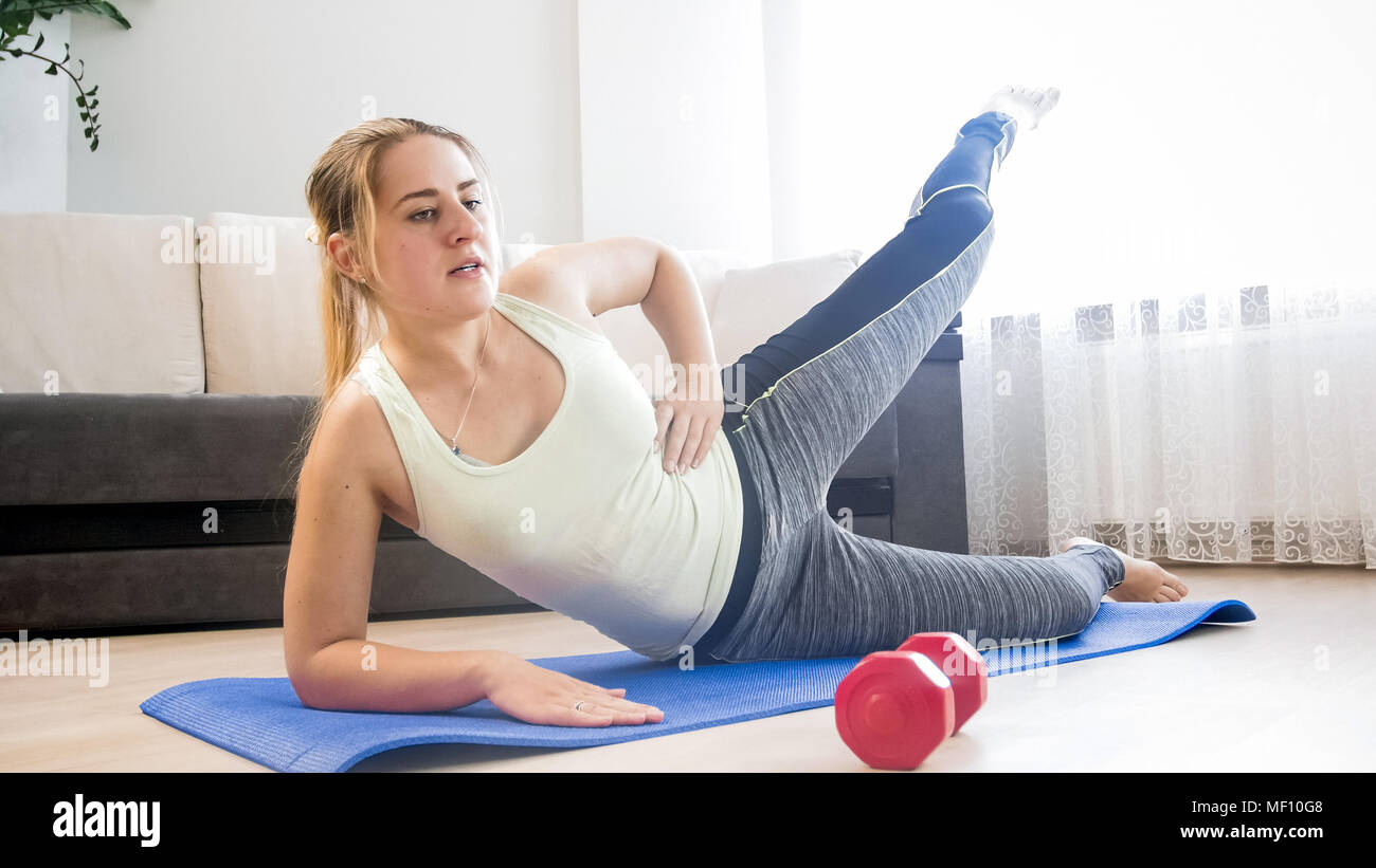 Young blonde woman lying on fitness mat and lifting leg up Stock Photo ...