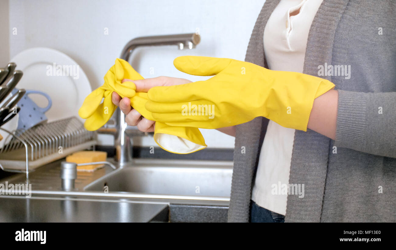 Closeup photo of young housewife taking off yellow latex gloves after washing dishes Stock Photo