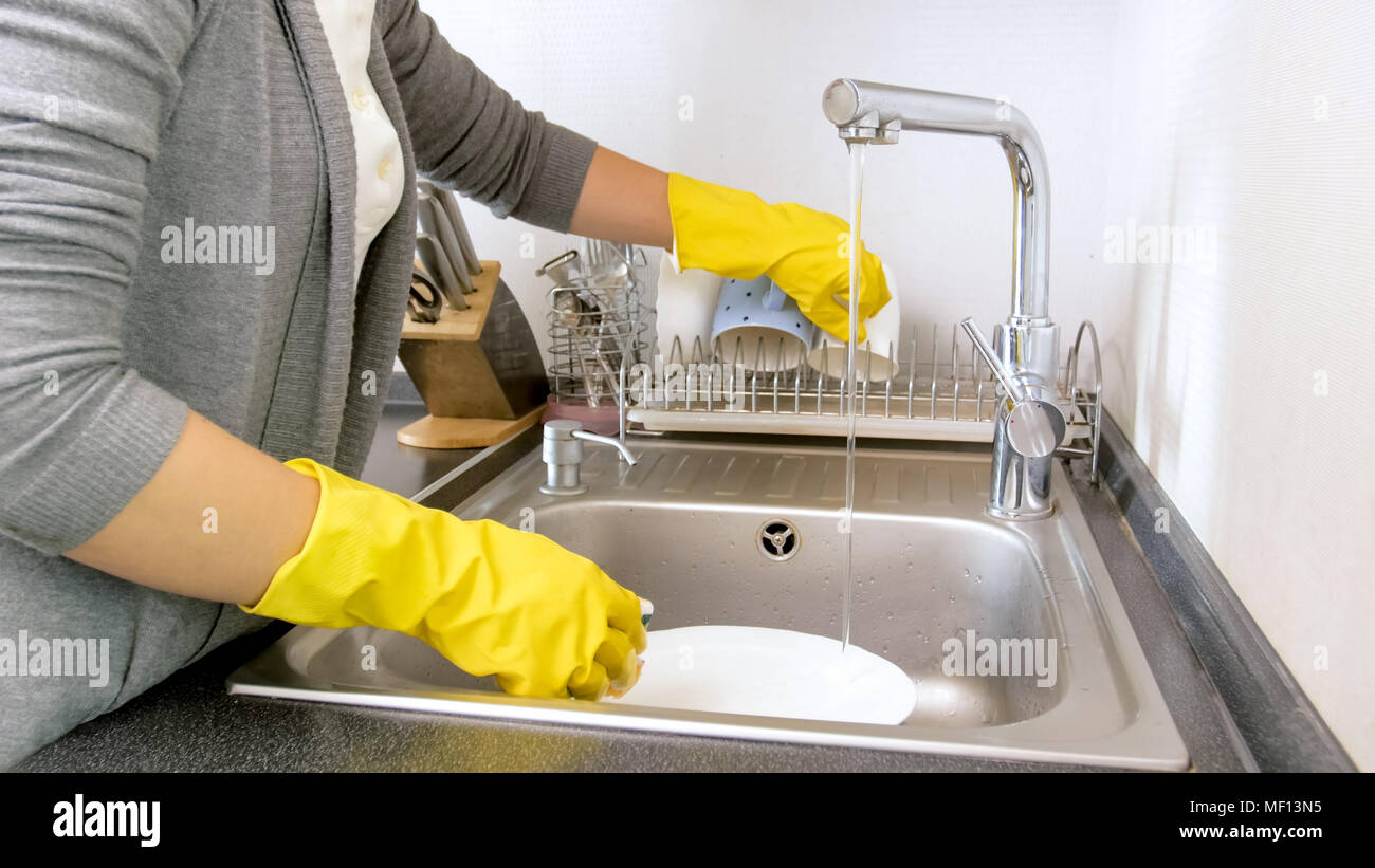 Closeup photo of female hands in yellow rubber gloves washing dishes ...