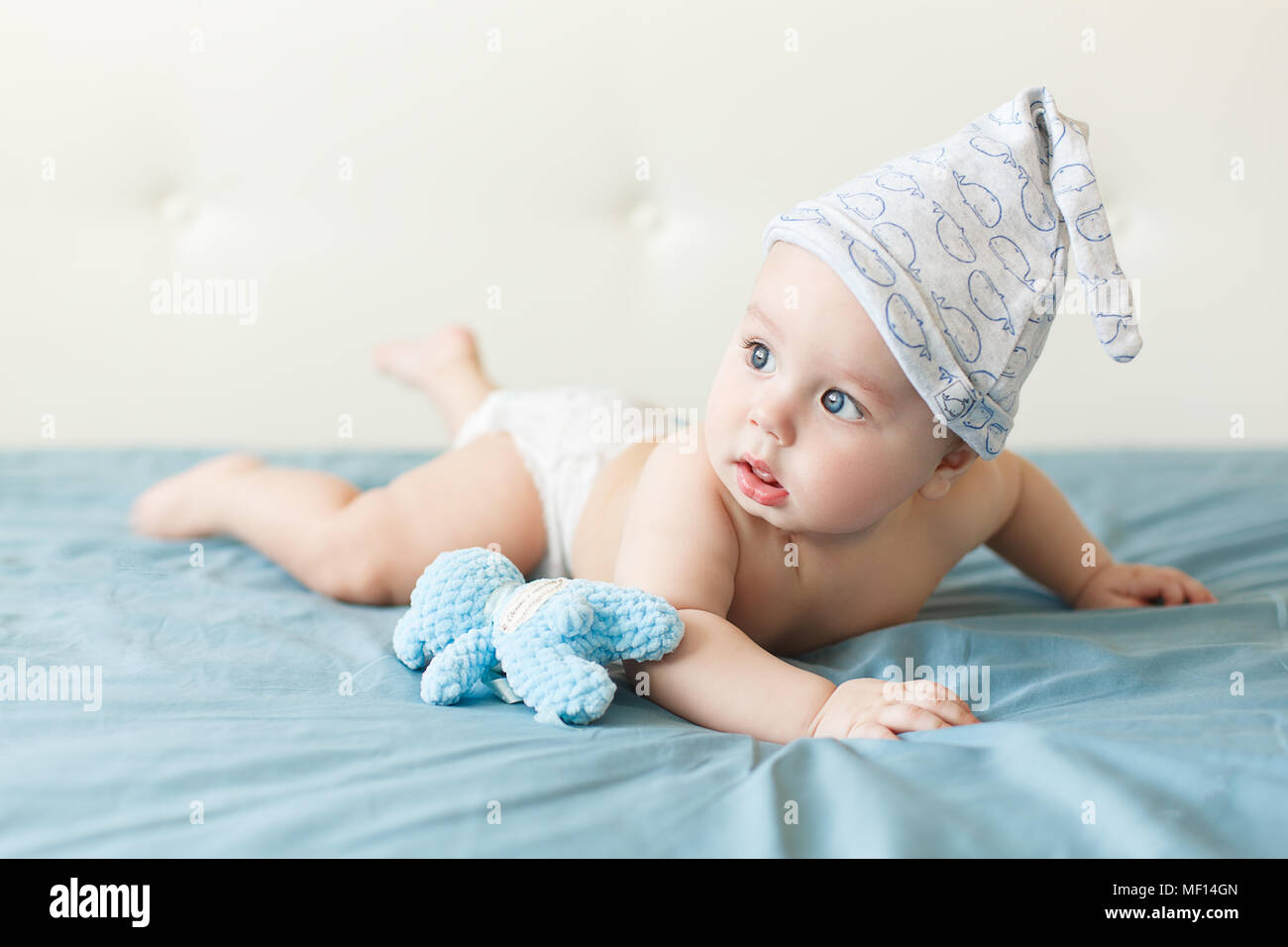 Little funny baby boy with big blue eyes smiling with cute cap on his head. Indoor Stock Photo