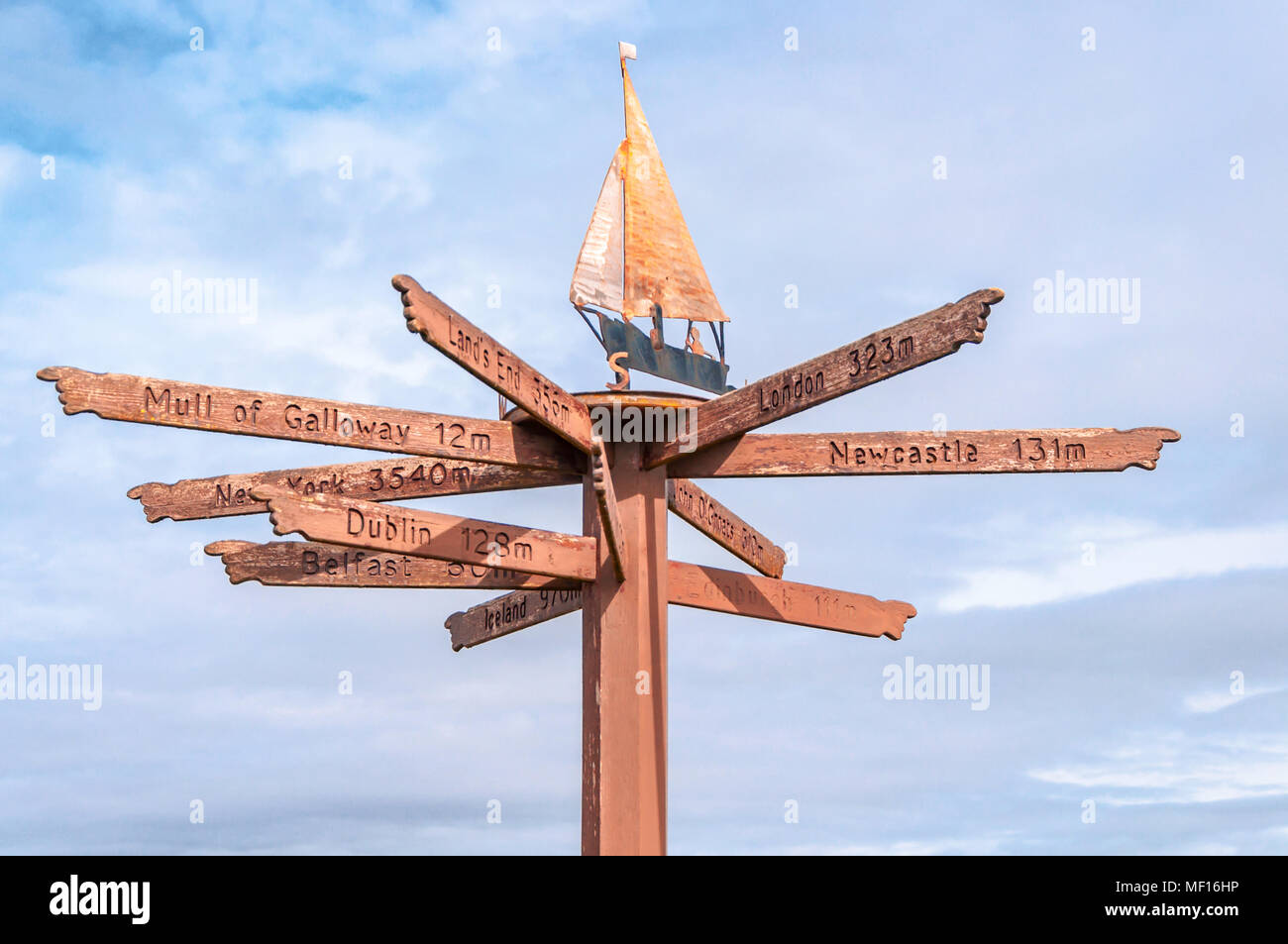 Tourist direction & distance signs mounted on post with weather vane on top, located on shorefront in Port William, Dumfries & Galloway, Scotland, UK Stock Photo