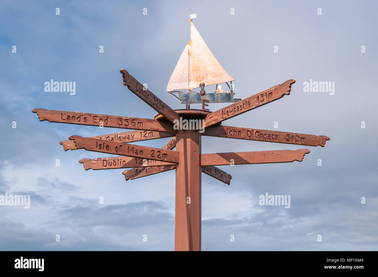 Tourist direction & distance signs mounted on post with weather vane on top, located on shorefront in Port William, Dumfries & Galloway, Scotland, UK Stock Photo