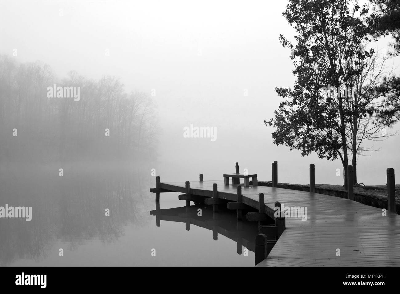 A thick blanket of fog covers a wooden deck and lake on a cold winter day. Stock Photo