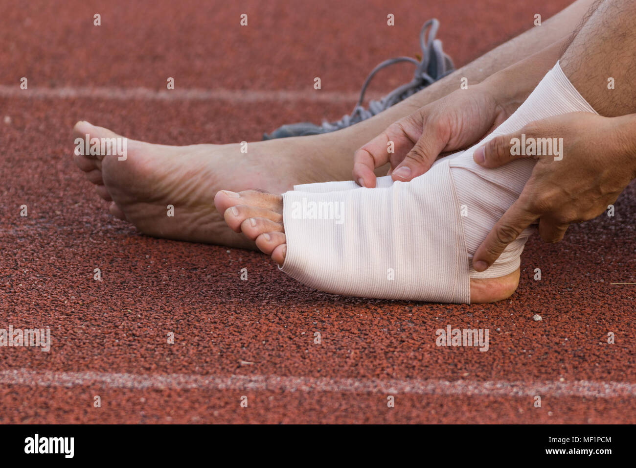 Male athlete applying compression bandage onto ankle injury of a