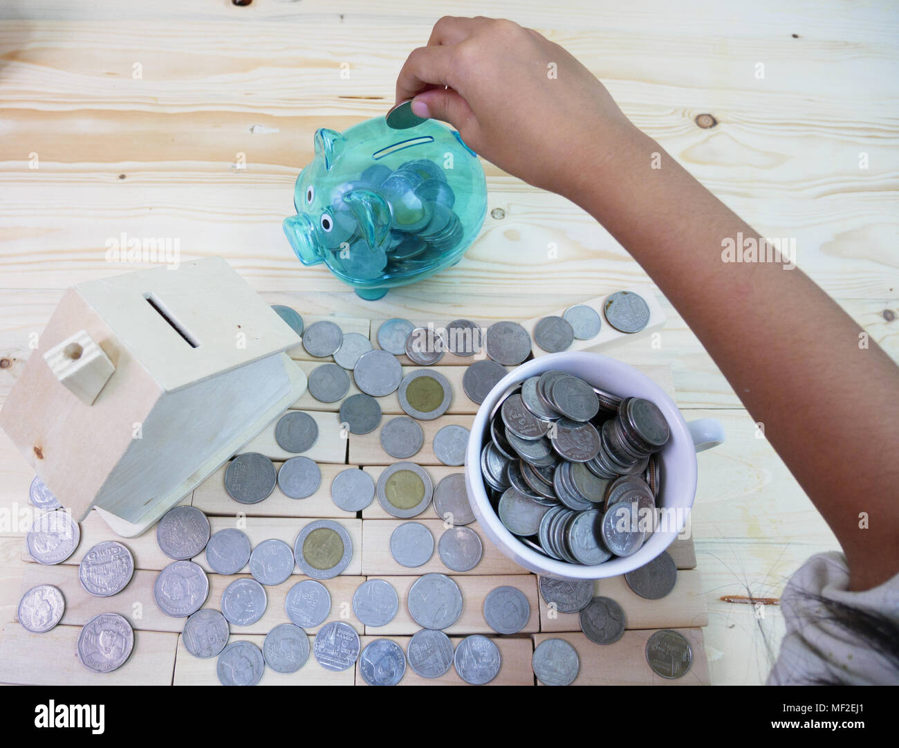 Drop coins in a piggy bank around a house and a glass of coins. Stock Photo