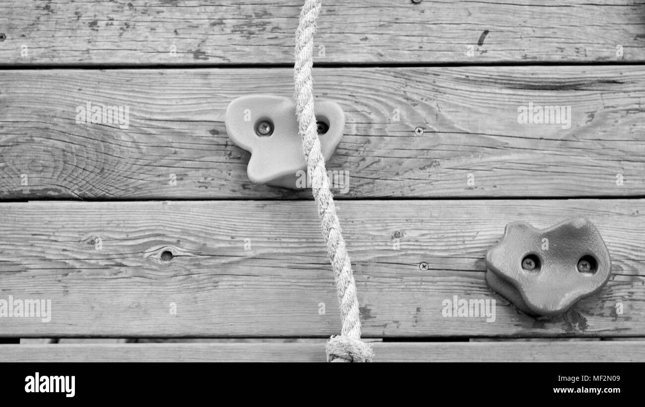 Black and white closeup image of wooden wall with rope and rocks for climbing Stock Photo